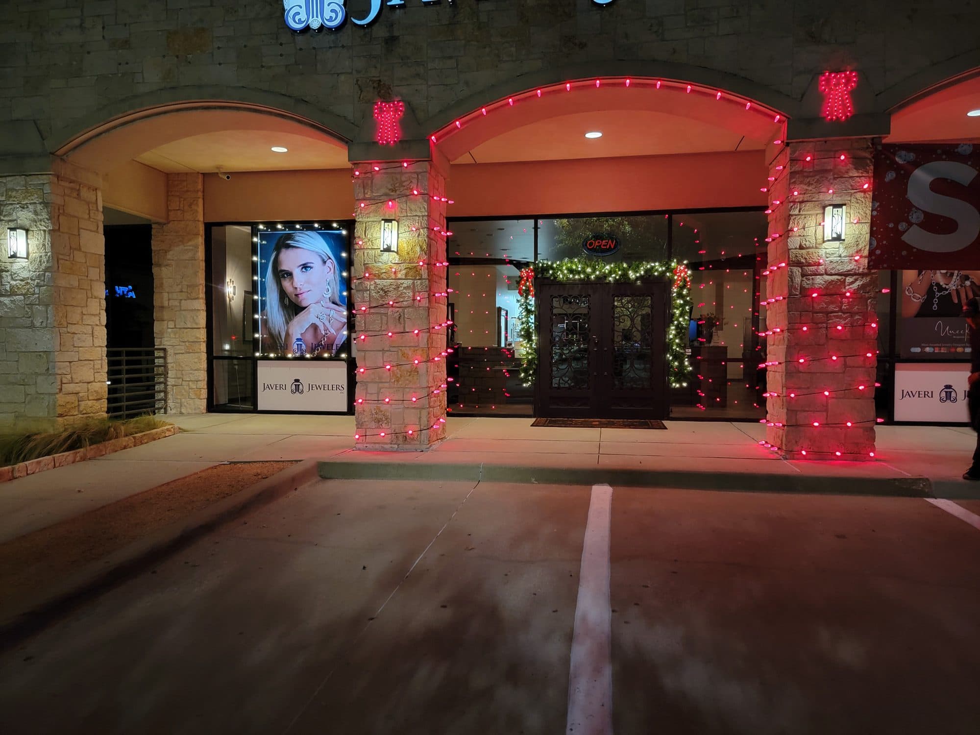 Javeri Jewelers storefront in Frisco with red C9 bulbs on the pillars and arch and pre-lit garland with red bows over the door