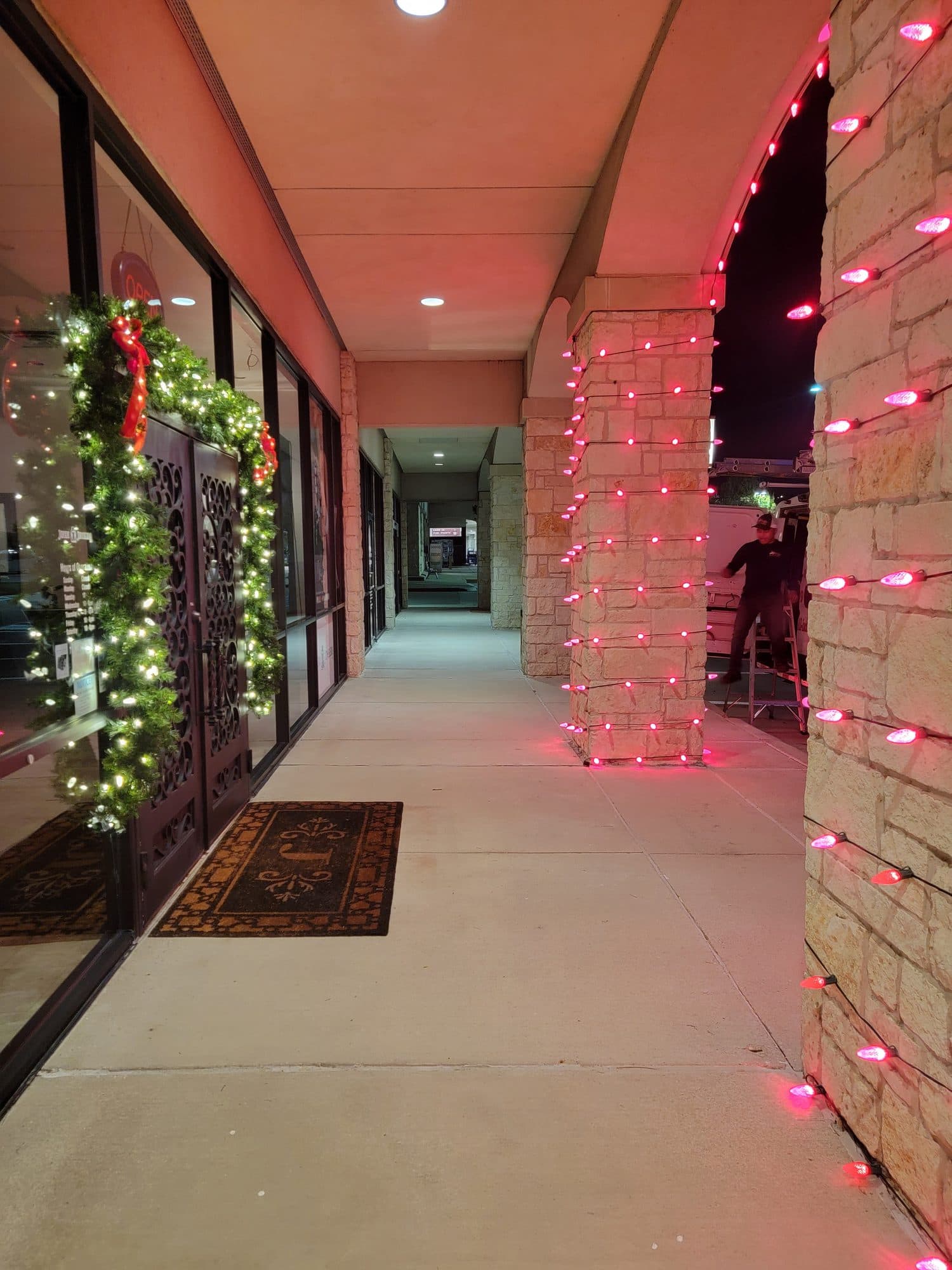 Covered walkway at Javeri Jewelers in Frisco with red C9 bulbs wrapped around the stone pillars and a garland-framed entry