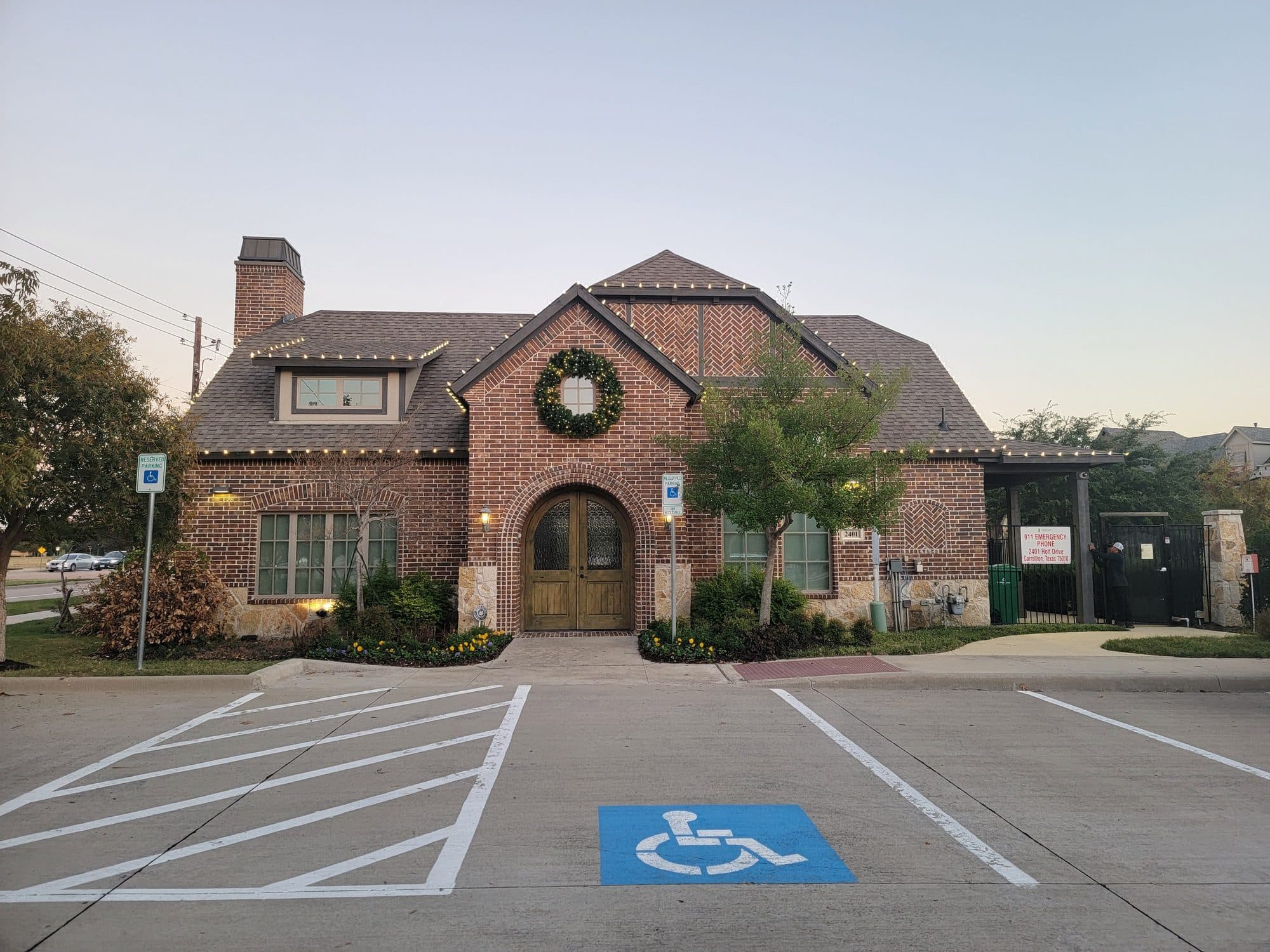 Mustang Park clubhouse in Carrollton with a pre-lit wreath above the arched entry and warm white lights along the roofline