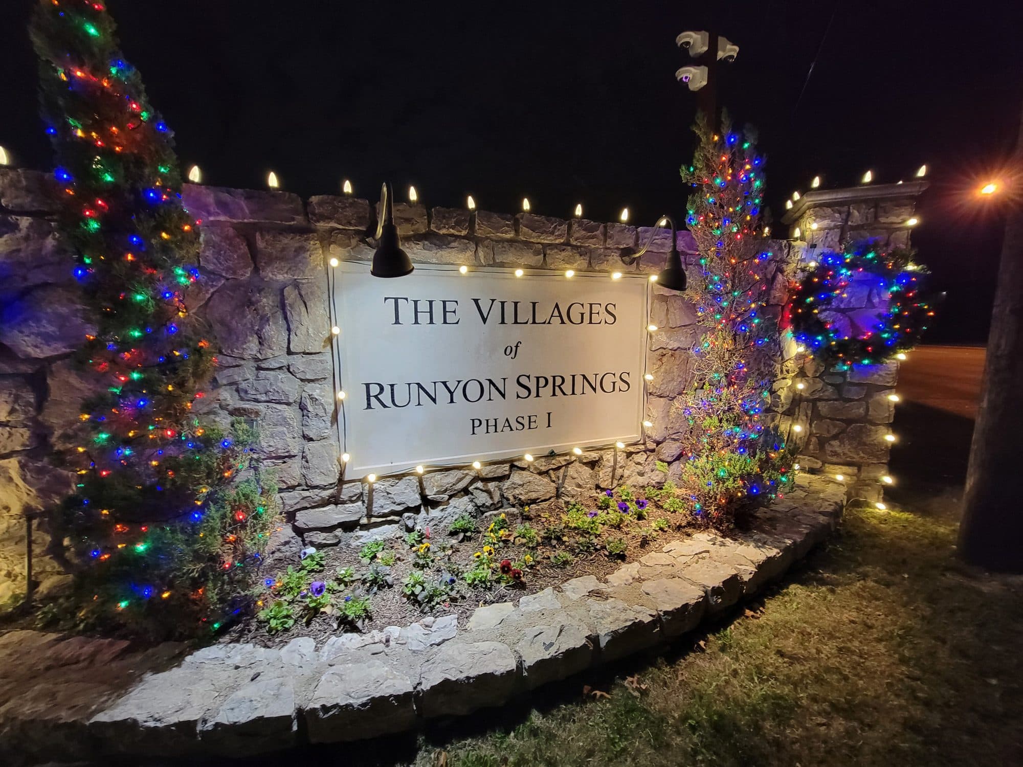 The Villages of Runyon Springs entrance monument in Dallas with warm white lights on the monument and multicolor mini lights on the entrance trees