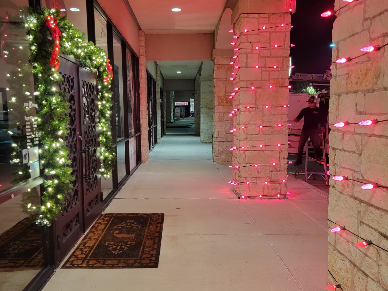 Storefront entrance framed in pre-lit garland with red mini lights